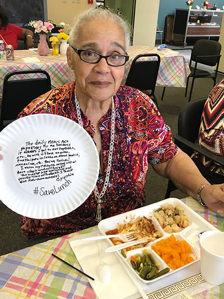 Rose Centers participant eating lunch and holding up a paper plate explaining why Rose Center meals matter for the  hashtag SaveLunch campaign