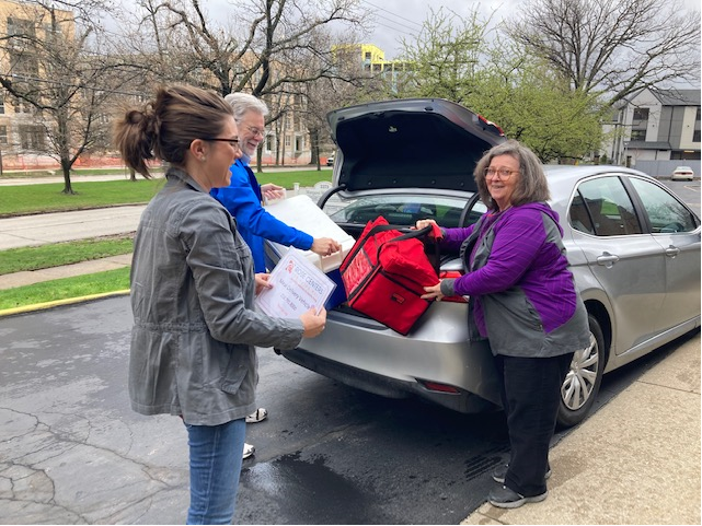 Three volunteers loading the trunk of a car with home-delivered meals for older adults