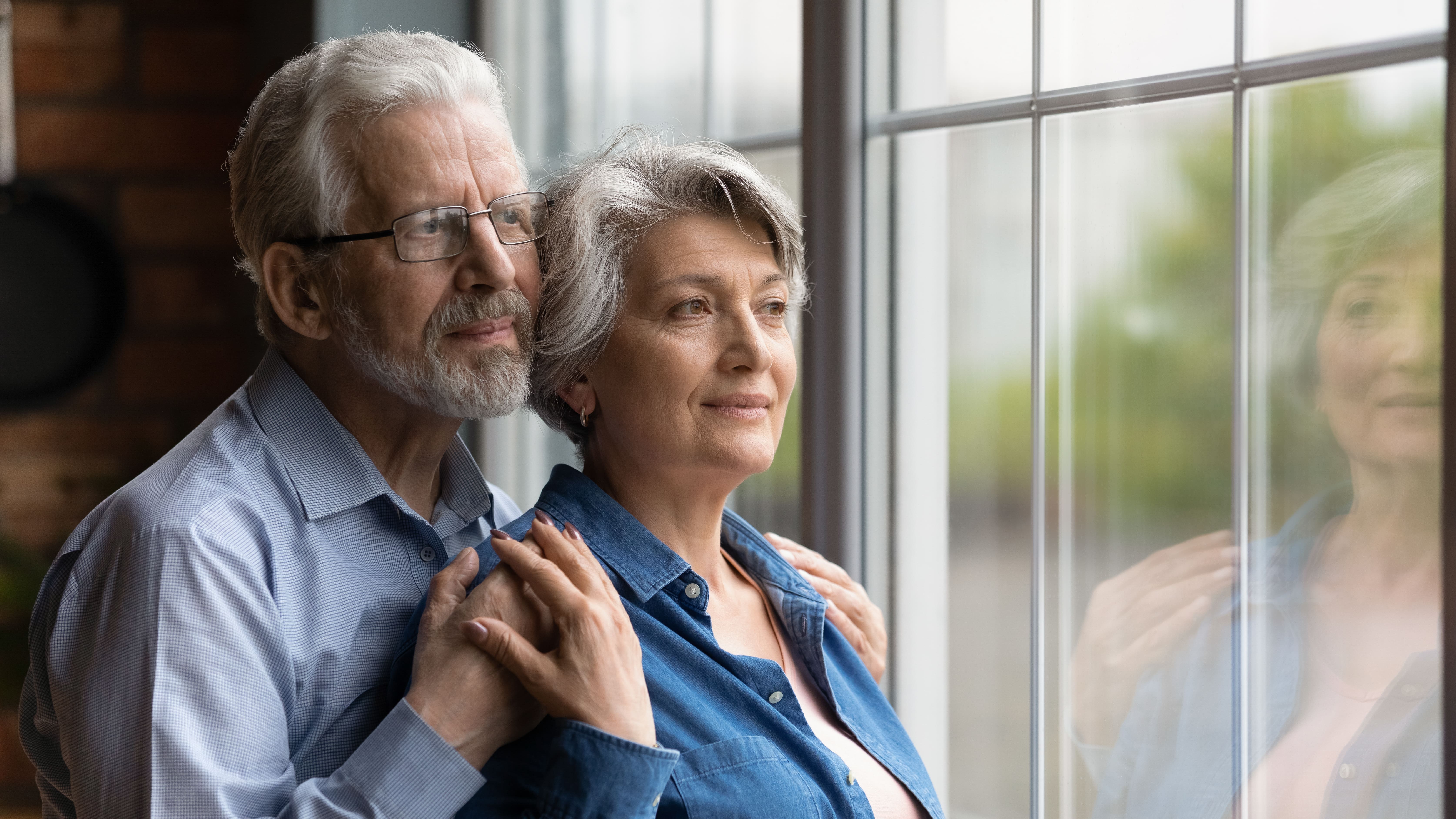 An older couple gazing out of a window together while embracing