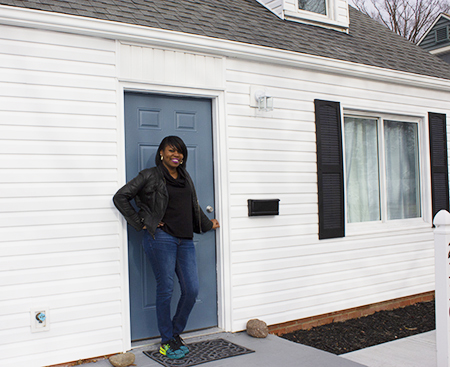 First time ESOP homeowner standing in front of a white house with a blue door while smiling