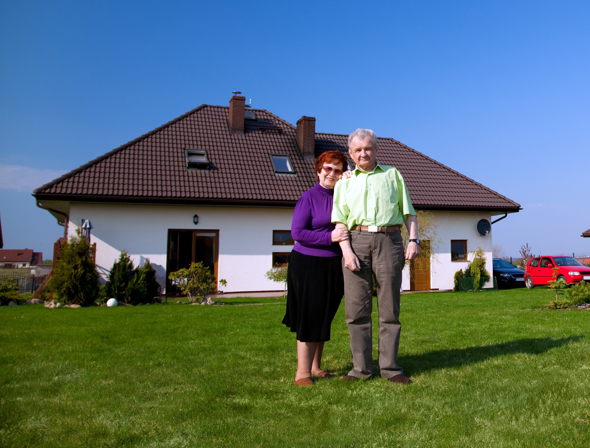 An older couple standing in front of their home