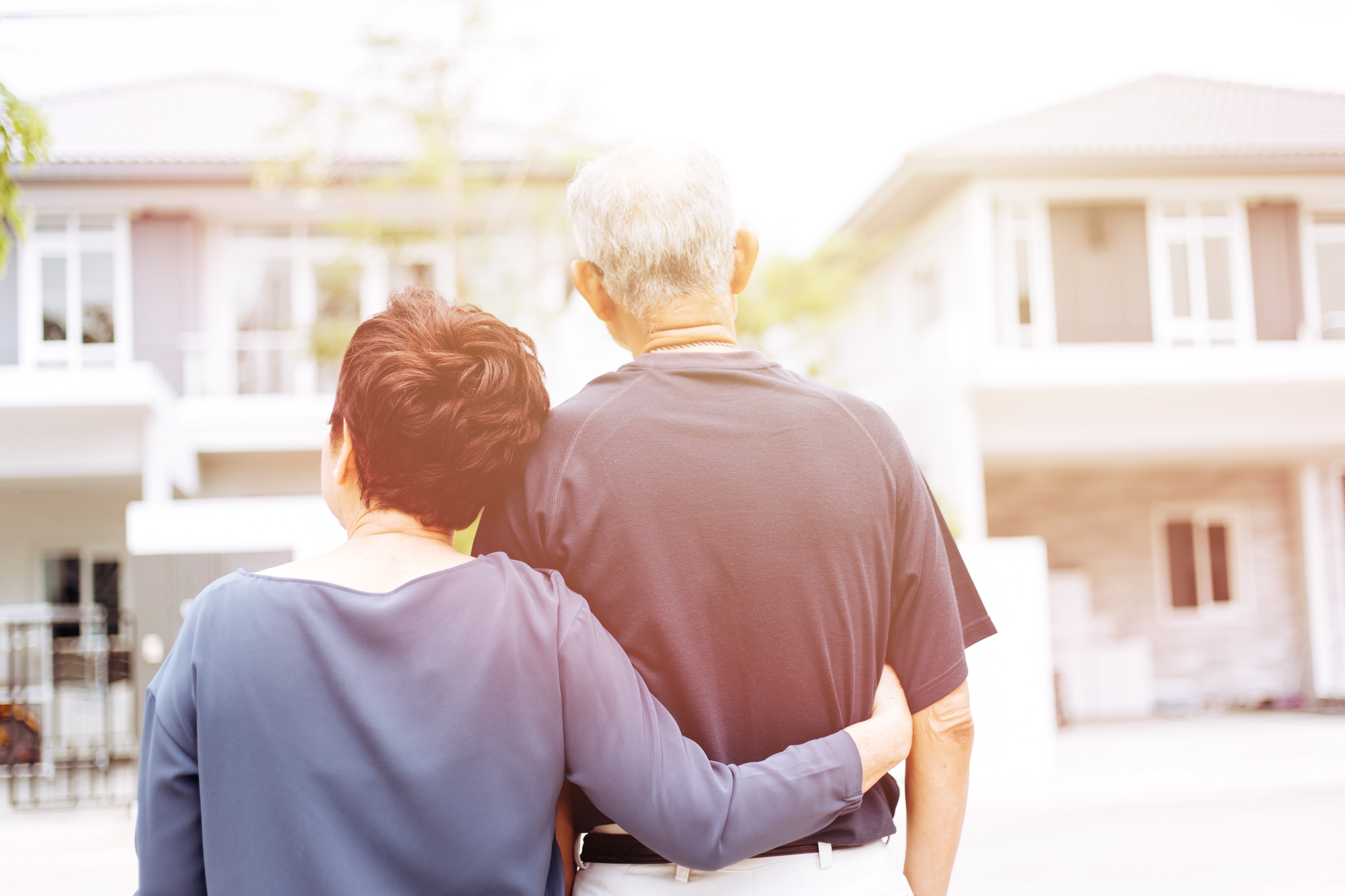 A backview of an older couple standing in front of their home