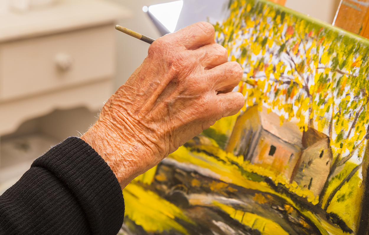 An older adult working on a landscape painting