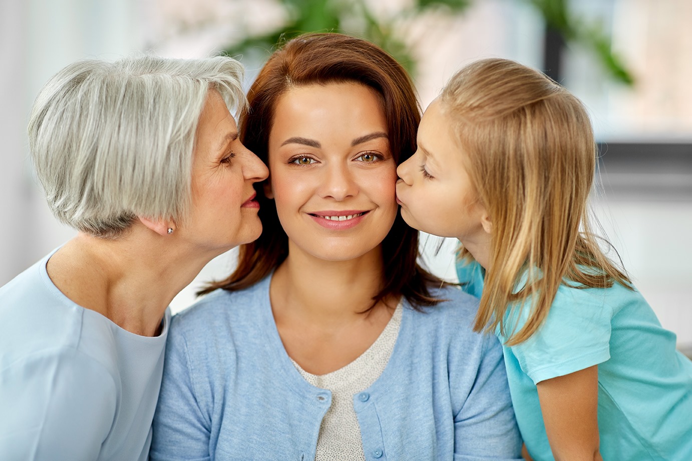 A caregiver being kissed on the cheek by her child and older loved one