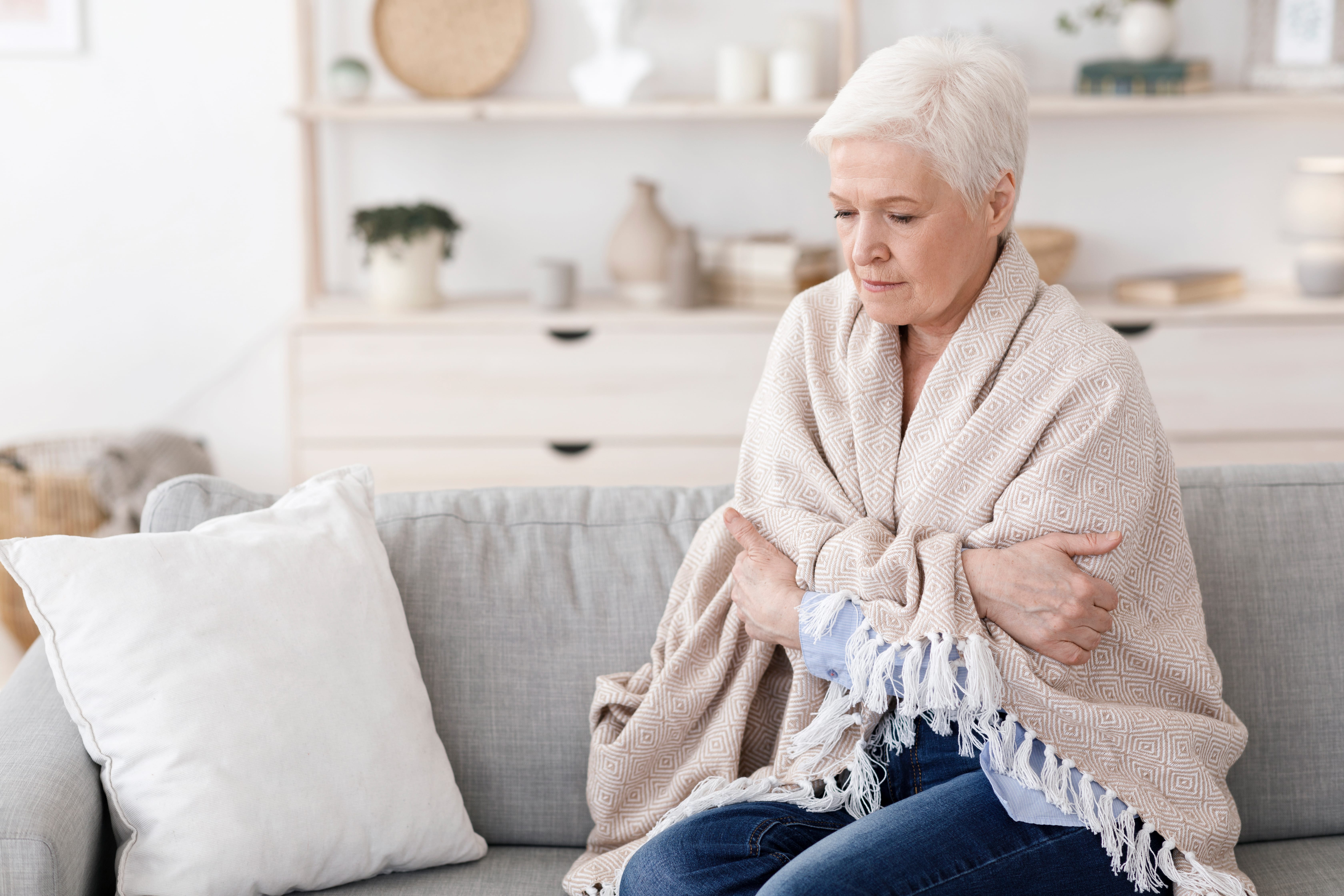 An older adult wrapping herself in a shawl to stay warm in the home