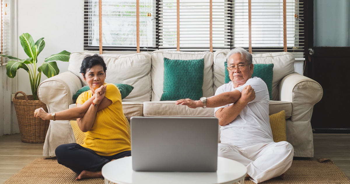 An older couple doing stretches in front of a laptop